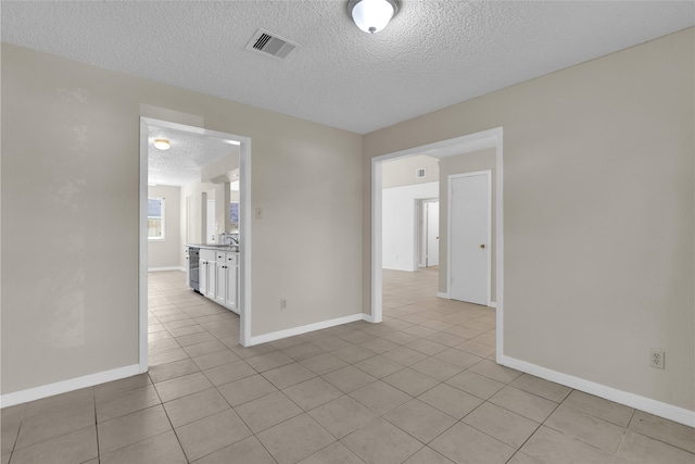 unfurnished room with visible vents, baseboards, light tile patterned flooring, a textured ceiling, and a sink