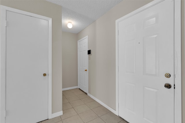 interior space with light tile patterned flooring, a textured ceiling, and baseboards