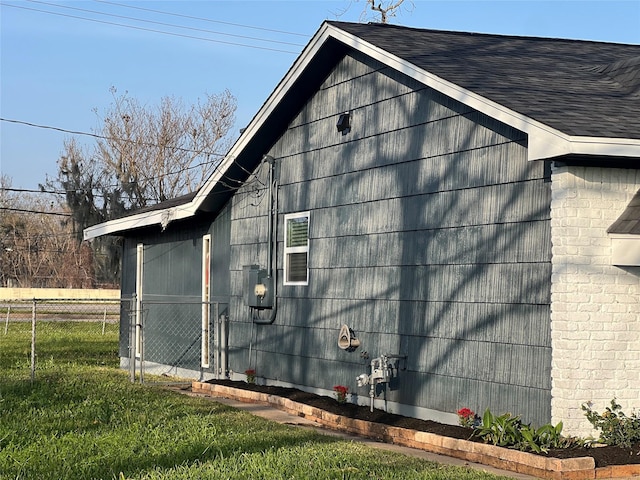 view of side of property with a lawn, roof with shingles, and fence