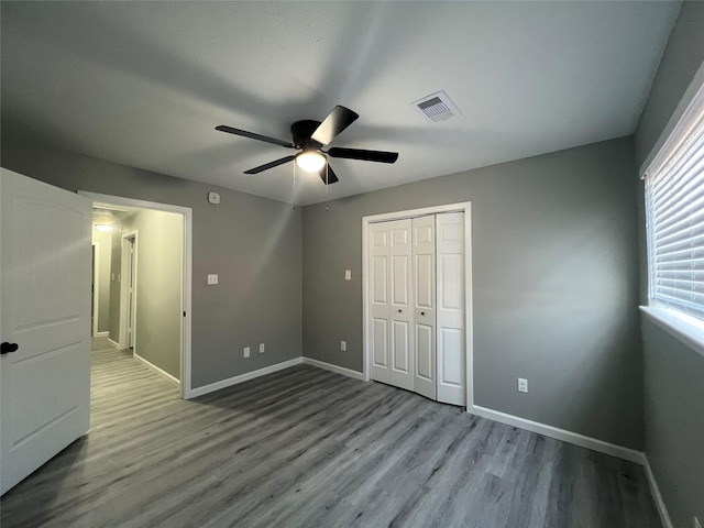 unfurnished bedroom featuring wood finished floors, visible vents, a closet, and baseboards