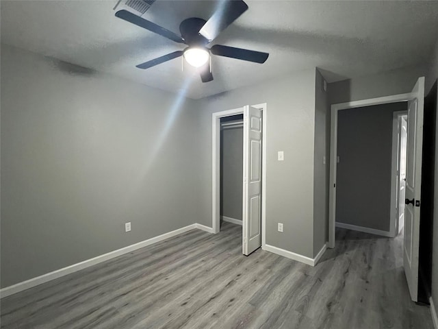 unfurnished bedroom with wood finished floors, baseboards, a closet, and ceiling fan