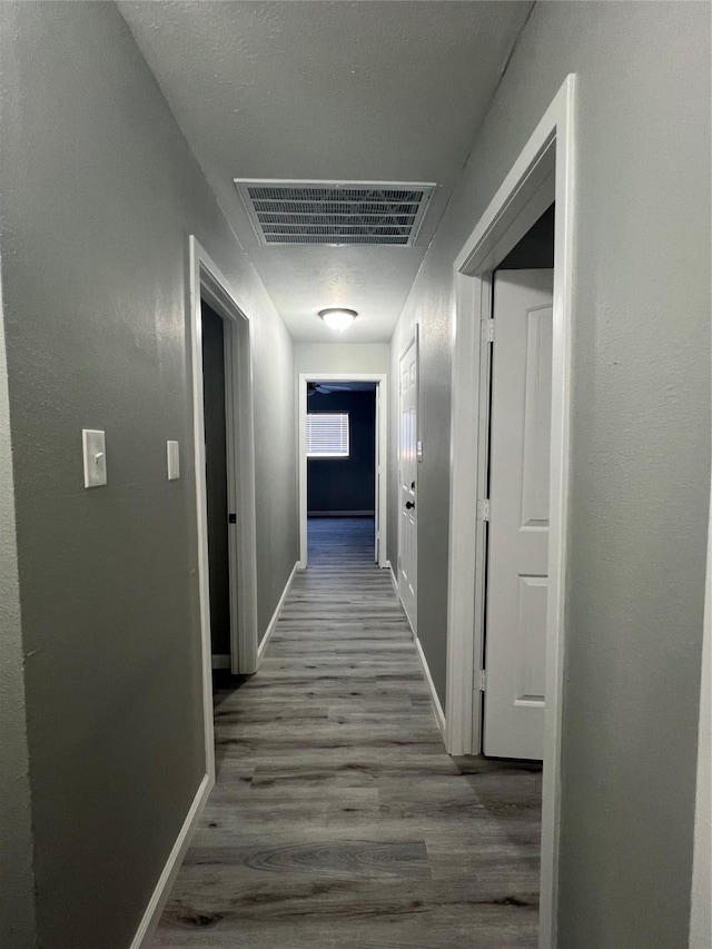 corridor featuring visible vents, dark wood-type flooring, and baseboards