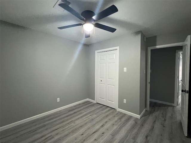 unfurnished bedroom featuring wood finished floors, baseboards, a closet, and ceiling fan