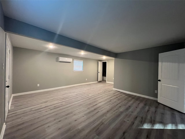 below grade area with an AC wall unit, baseboards, and wood finished floors