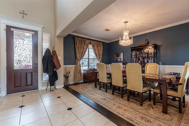 dining area with tile patterned floors, visible vents, ornamental molding, an inviting chandelier, and wainscoting