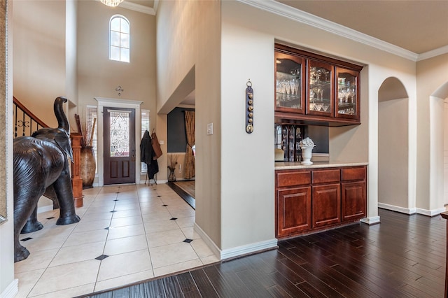 entryway featuring baseboards, arched walkways, light wood-style floors, and crown molding