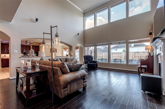 living room with arched walkways, dark wood-type flooring, a healthy amount of sunlight, and ornamental molding