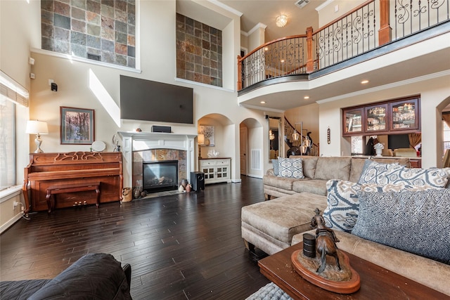 living area featuring arched walkways, ornamental molding, a tiled fireplace, and hardwood / wood-style floors