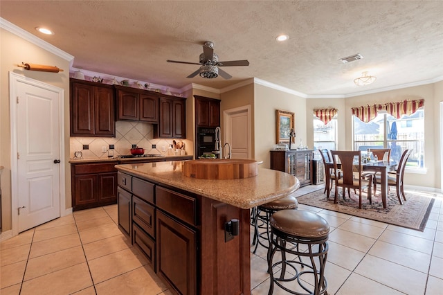 kitchen with light tile patterned floors, a center island with sink, visible vents, a breakfast bar, and tasteful backsplash