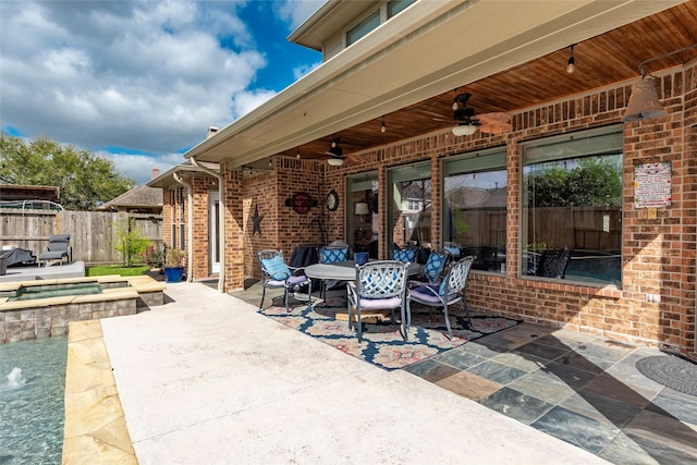 view of patio / terrace featuring an in ground hot tub, outdoor dining space, a ceiling fan, and fence