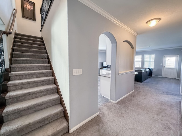 staircase featuring baseboards, carpet, arched walkways, and ornamental molding