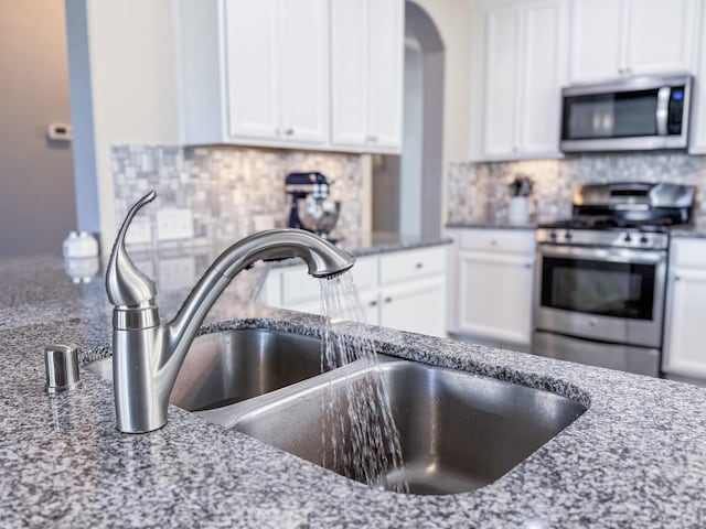 kitchen featuring white cabinets, light stone counters, tasteful backsplash, and appliances with stainless steel finishes