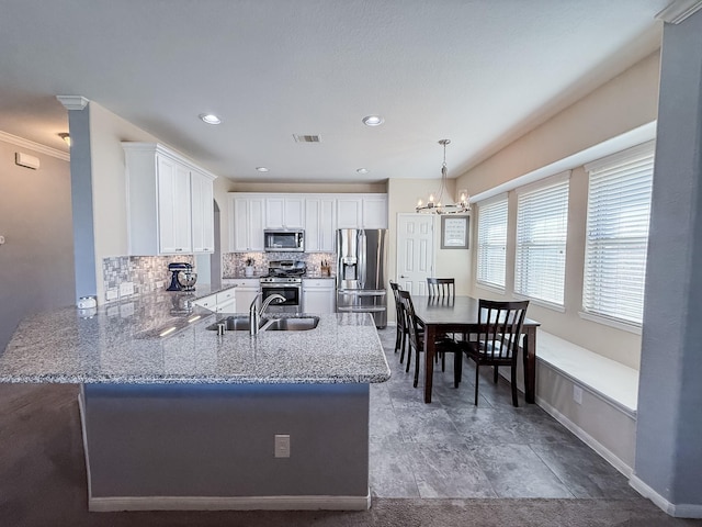 kitchen featuring tasteful backsplash, a chandelier, appliances with stainless steel finishes, a peninsula, and a sink