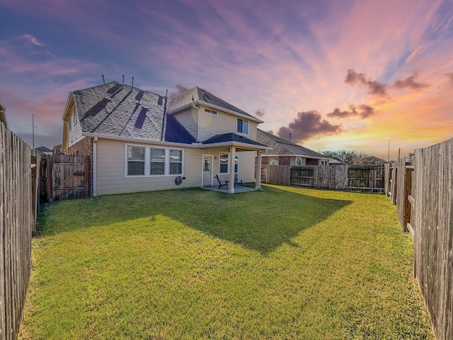 back of house at dusk featuring a shingled roof, a lawn, a fenced backyard, and a patio area