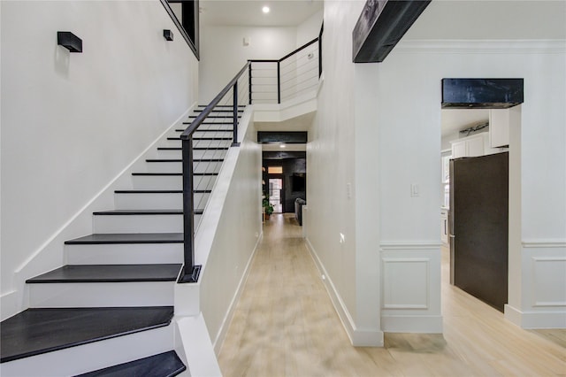 stairs with a wainscoted wall, wood finished floors, a high ceiling, crown molding, and a decorative wall