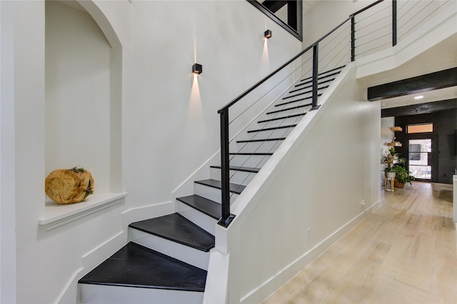 staircase with baseboards, beamed ceiling, a high ceiling, wood finished floors, and arched walkways