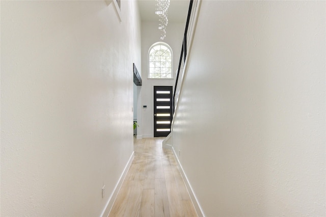 hallway with light wood finished floors, baseboards, a towering ceiling, and a chandelier