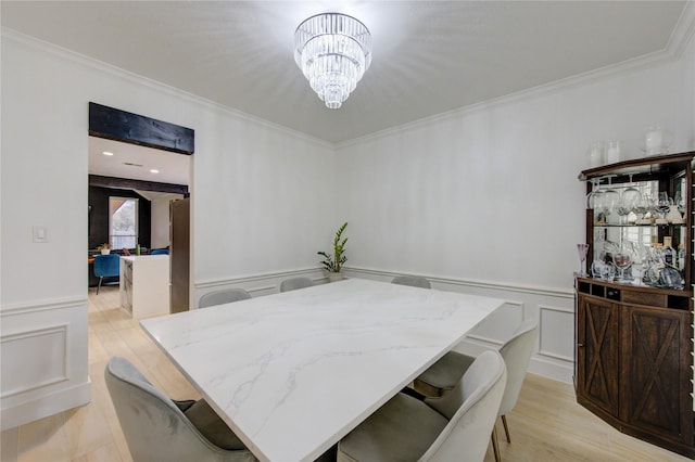 dining area with light wood finished floors, crown molding, a wainscoted wall, an inviting chandelier, and a decorative wall