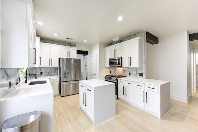 kitchen featuring a kitchen island, light wood-type flooring, light countertops, appliances with stainless steel finishes, and a sink