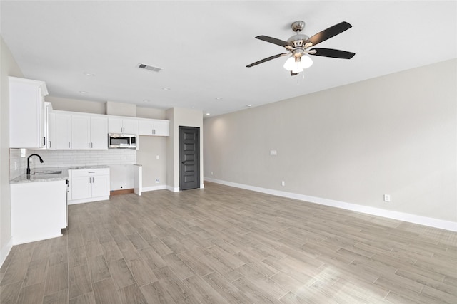 unfurnished living room featuring light wood finished floors, visible vents, baseboards, a ceiling fan, and a sink