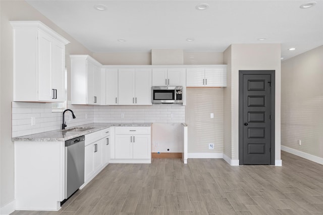 kitchen featuring tasteful backsplash, light stone counters, appliances with stainless steel finishes, white cabinets, and a sink