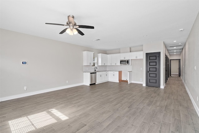 unfurnished living room with visible vents, baseboards, light wood-style flooring, ceiling fan, and a sink