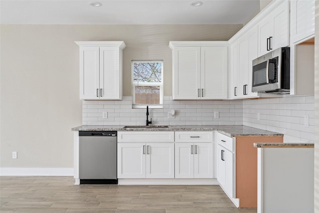 kitchen with light stone counters, a sink, appliances with stainless steel finishes, white cabinetry, and tasteful backsplash