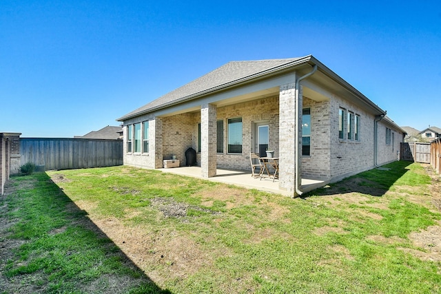 back of house featuring a yard, a patio, brick siding, and a fenced backyard