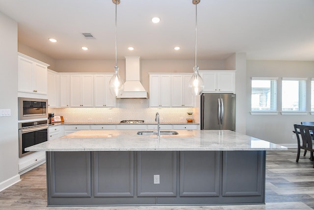 kitchen featuring visible vents, custom exhaust hood, a large island with sink, a sink, and appliances with stainless steel finishes