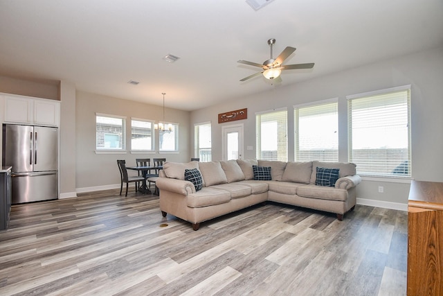 living room with visible vents, baseboards, light wood-style flooring, and ceiling fan with notable chandelier