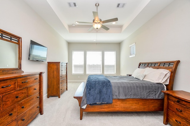 bedroom featuring a tray ceiling, visible vents, light carpet, and baseboards