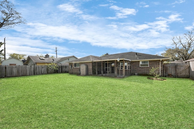 rear view of house featuring a sunroom, a lawn, brick siding, and a fenced backyard