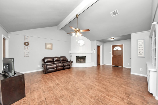 living area featuring a ceiling fan, visible vents, light wood finished floors, lofted ceiling with beams, and a fireplace with raised hearth