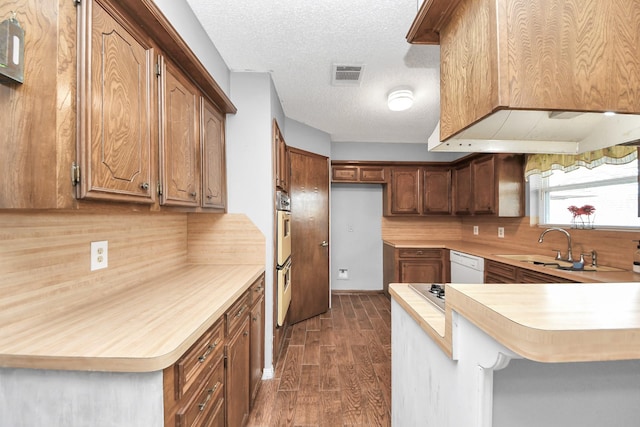 kitchen featuring visible vents, a sink, dark wood finished floors, white dishwasher, and light countertops