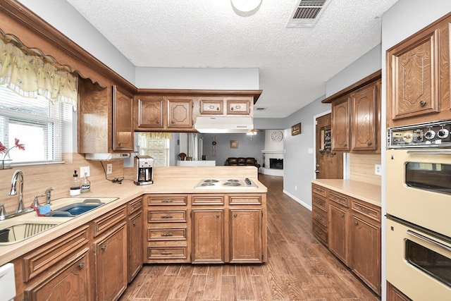 kitchen featuring white appliances, light wood finished floors, a peninsula, light countertops, and tasteful backsplash