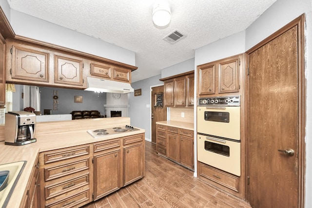 kitchen with light wood finished floors, visible vents, white double oven, under cabinet range hood, and light countertops