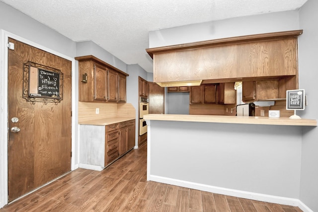 kitchen featuring a textured ceiling, wood finished floors, a peninsula, light countertops, and white double oven