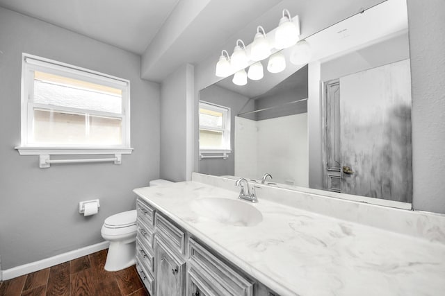 bathroom featuring toilet, wood finished floors, baseboards, walk in shower, and vanity