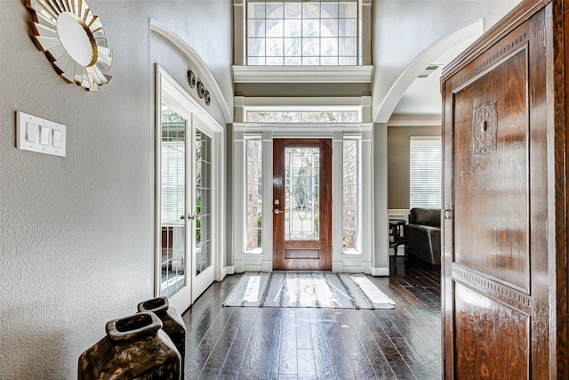 entrance foyer featuring hardwood / wood-style floors, visible vents, arched walkways, a towering ceiling, and a textured wall