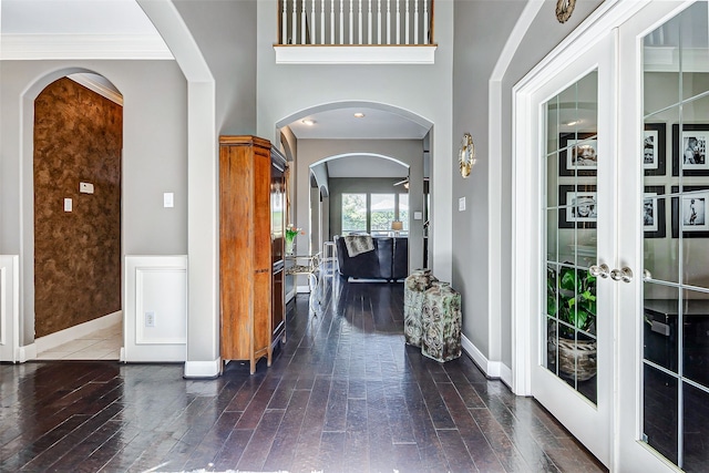 foyer entrance featuring french doors, arched walkways, baseboards, and wood finished floors