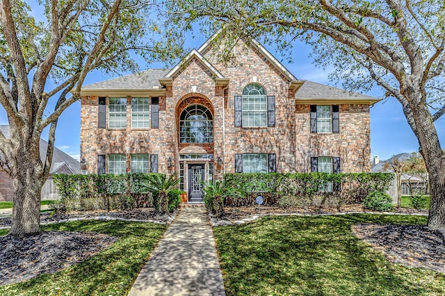 traditional-style home with a front yard, brick siding, and a shingled roof