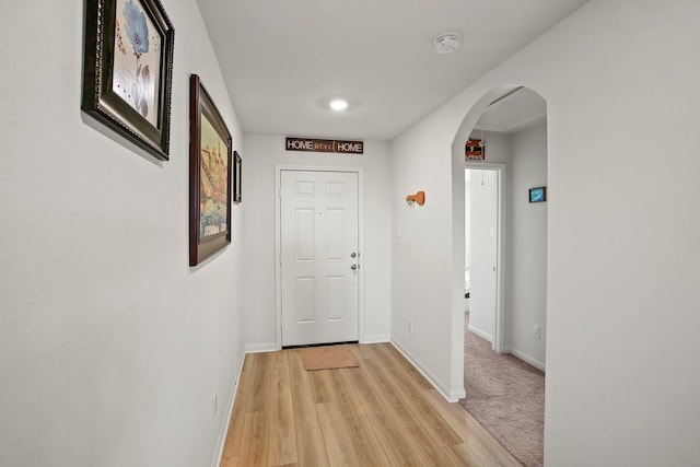 hallway featuring arched walkways, light wood-style flooring, and baseboards