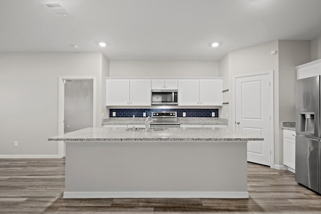 kitchen with a kitchen island with sink, wood finished floors, white cabinetry, appliances with stainless steel finishes, and decorative backsplash