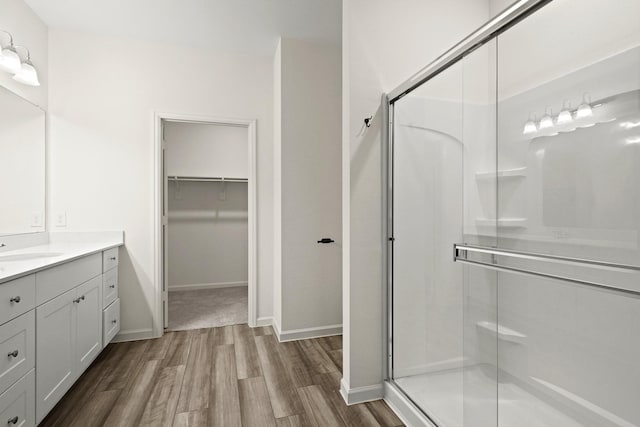 bathroom featuring vanity, wood finished floors, baseboards, a shower stall, and a spacious closet