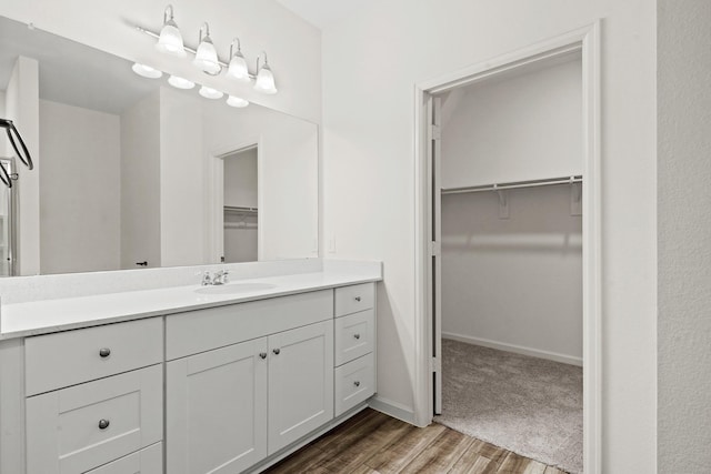 bathroom with baseboards, vanity, wood finished floors, and a spacious closet