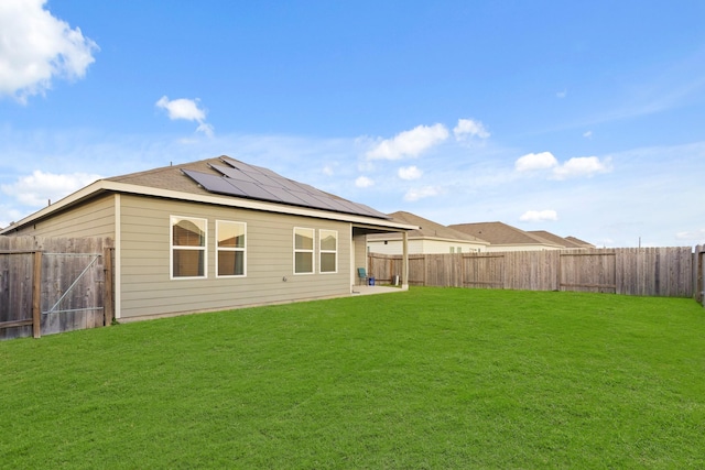 back of property featuring roof mounted solar panels, a lawn, and a fenced backyard