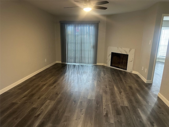 unfurnished living room featuring a premium fireplace, baseboards, dark wood-type flooring, and a ceiling fan