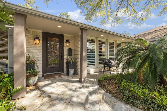 property entrance featuring a porch and brick siding