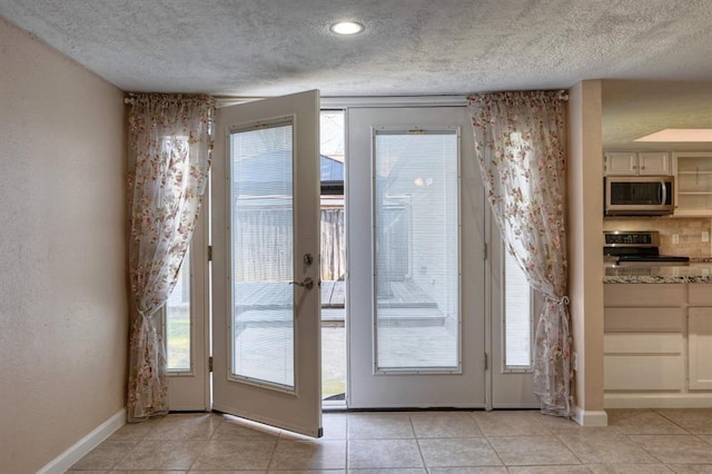 doorway to outside featuring light tile patterned floors, a textured wall, baseboards, and a textured ceiling