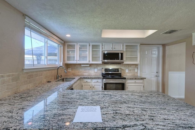 kitchen featuring light stone countertops, visible vents, a sink, stainless steel appliances, and white cabinets